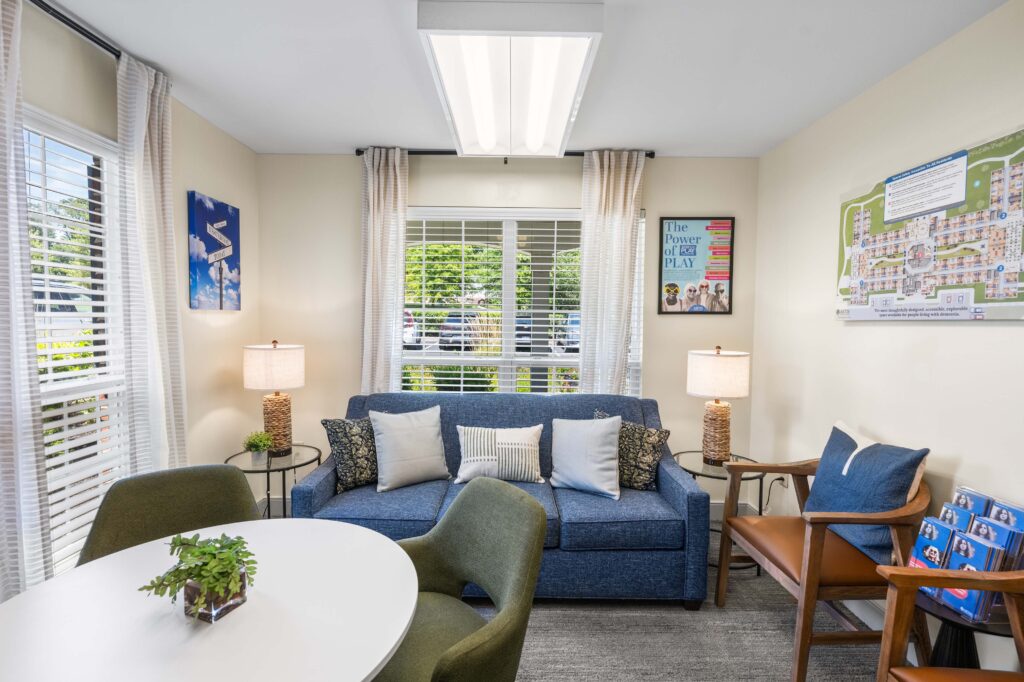 Welcome lounge at Artis Senior Living of Huntingdon Valley with a blue sofa, armchairs, a community map, and informational brochures.