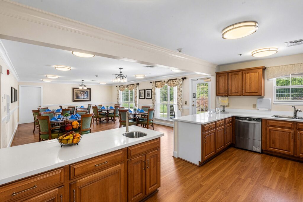 Open kitchen and dining room at Artis Senior Living of Huntingdon Valley with wood cabinetry, an island, and set tables in the background.