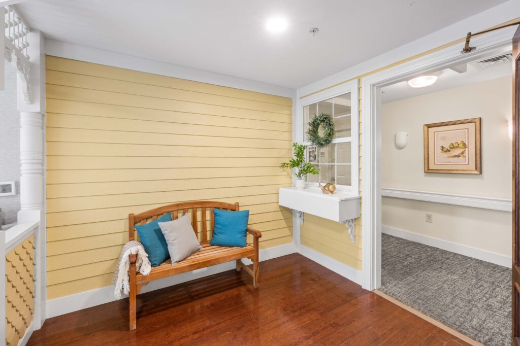 Indoor porch-themed nook at Artis Senior Living of Huntingdon Valley with a wooden bench, decorative window box, and faux siding walls.