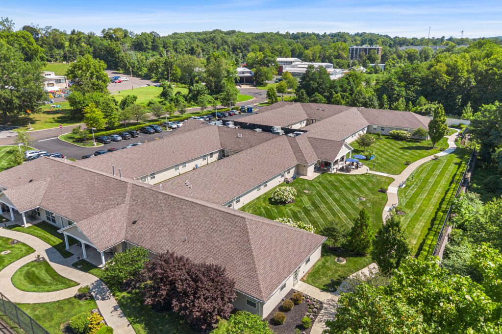 Daytime aerial view of Artis Senior Living of Huntingdon Valley showing multiple connected single-story buildings, courtyards, walking paths, and surrounding green lawns.