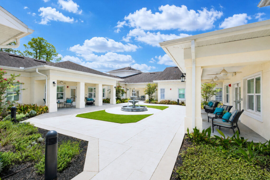 Enclosed courtyard at Artis Senior Living of Palm Coast with a fountain, covered porch seating, and direct access to resident rooms