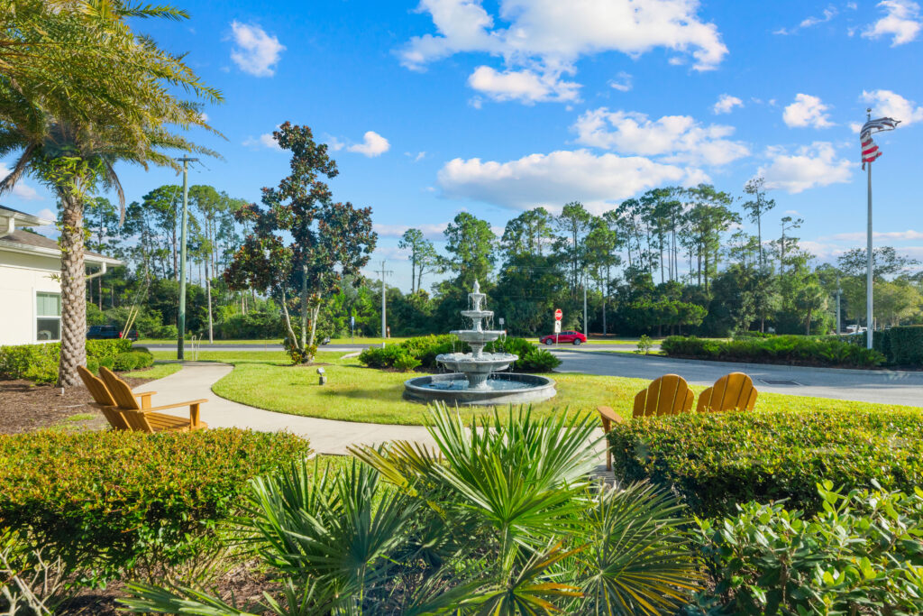 Outdoor courtyard at Artis Senior Living of Palm Coast with a tiered fountain, Adirondack chairs, and landscaped grounds