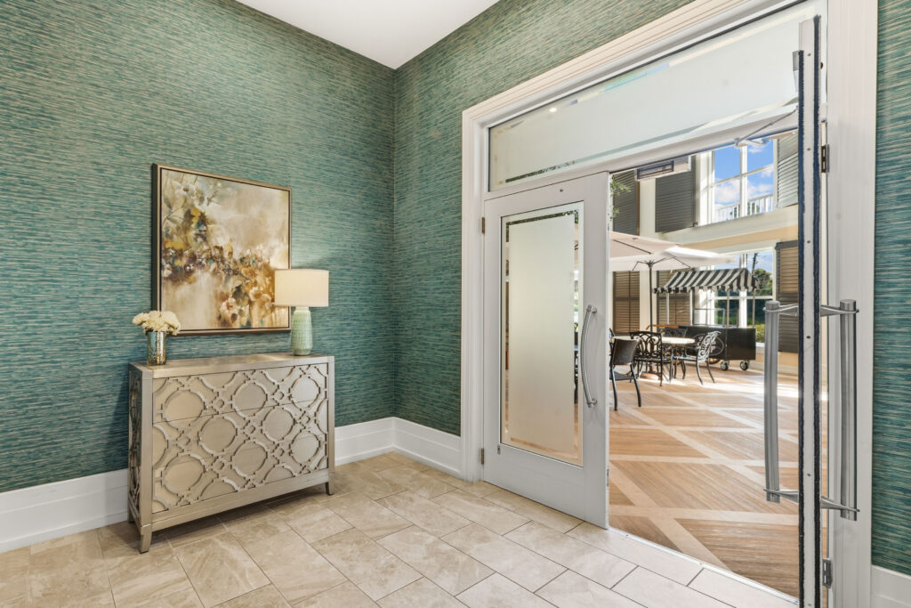 Hallway with teal textured walls at Artis Senior Living of Palm Coast, with a doorway opening onto the indoor courtyard