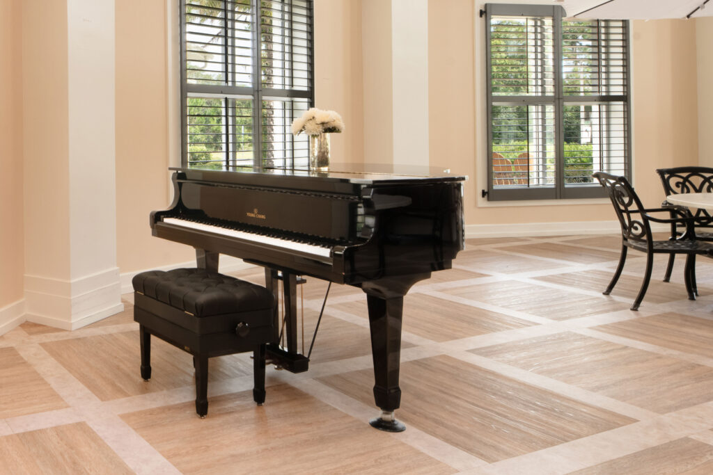 "A black grand piano near tall shuttered windows in a common area at Artis Senior Living of Palm Coast