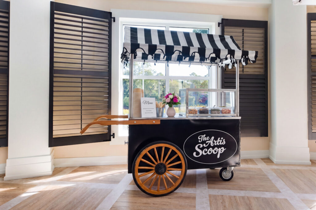 The Artis Scoop, a vintage-style ice cream cart with toppings and a striped awning, at Artis Senior Living of Palm Coast