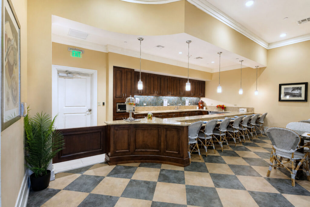 Bistro-style café at Artis Senior Living of Palm Coast with a long granite bar, counter seating, and pendant lighting