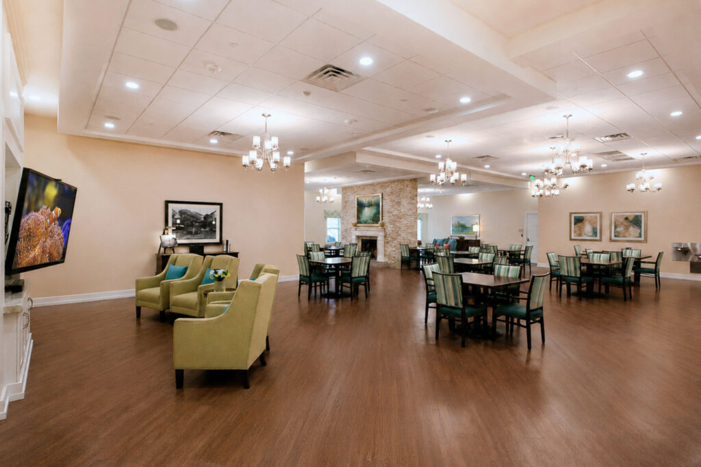 Spacious community gathering room at Artis Senior Living of Palm Coast with a TV lounge, stone fireplace, and multiple seating areas