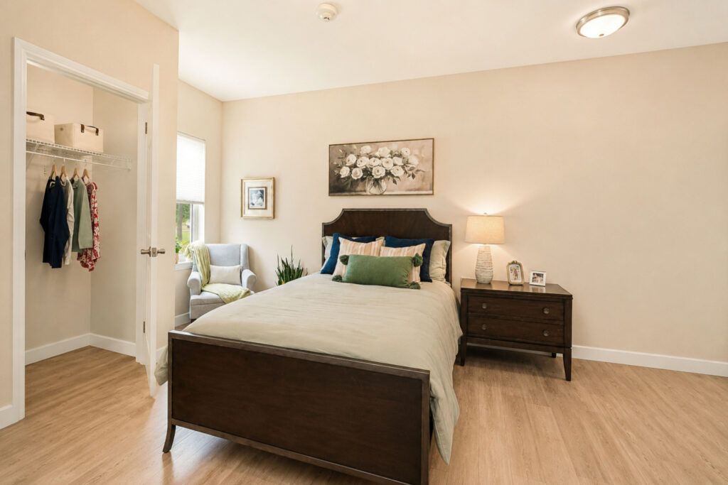 Private memory care bedroom at Artis Senior Living of Palm Coast with a dark wood bed, walk-in closet, reading chair, and nightstand with family photos