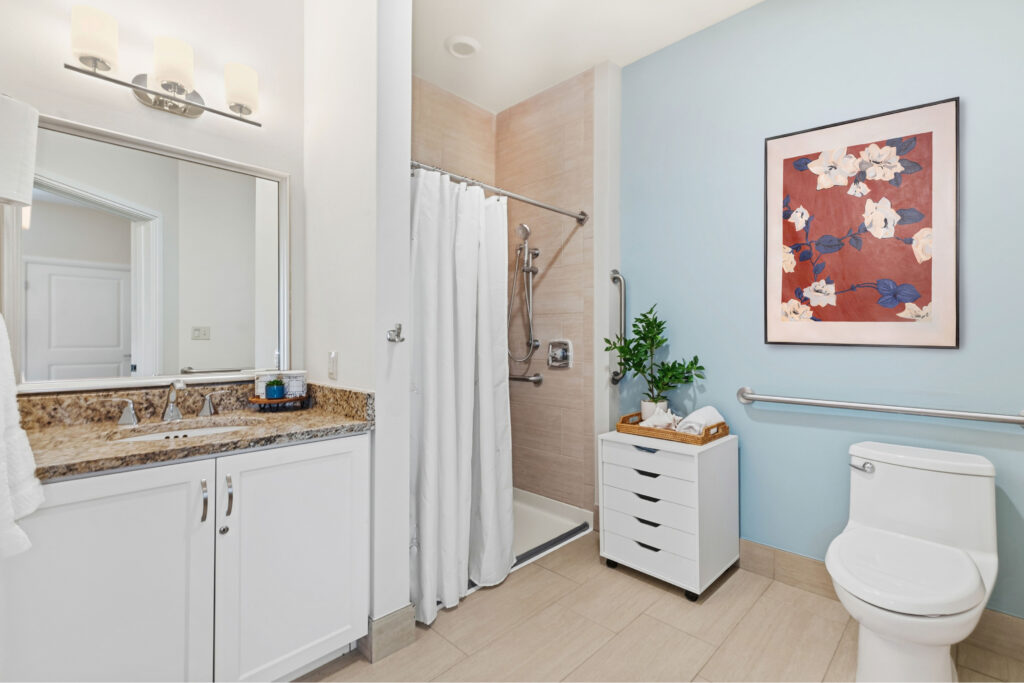 Private accessible bathroom at Artis Senior Living of Palm Coast with a curbless roll-in shower, grab bars, and granite vanity