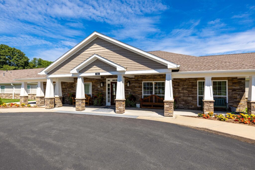 "Front entrance of Artis Senior Living of Branford at 814, a single-story craftsman-style building with stone accents, white columns, and a covered porch under a clear blue sky